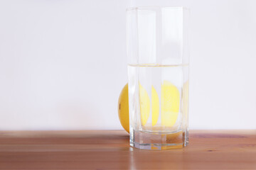 Glass of water and whole lemon is standing on the wooden desk. White background.