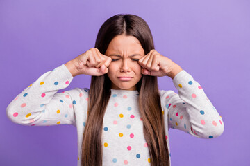 Photo portrait of sad crying child wiping tears with hands fists isolated on bright purple colored...