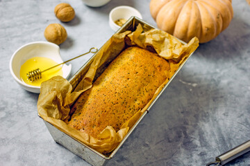 Homemade pumpkin cake with honey, poppy seeds, dried fruits, baked nuts and parchment paper, close-up. Healthy and delicious sugar-free cake recipe, next to baking ingredients. Homemade baking concept