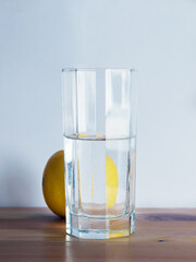 Glass of water and whole lemon is standing on the wooden desk. White background. Vertical orientation