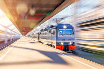 The lead electric locomotive with a passenger train passes at high speed through the city platform at the station.