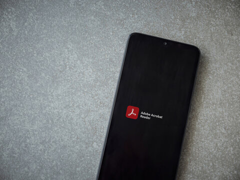 Lod, Israel - July 8, 2020: Adobe Acrobat Reader app launch screen with logo on the display of a black mobile smartphone on ceramic stone background. Top view flat lay with copy space.