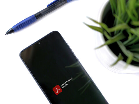 Modern minimalist office workspace with black mobile smartphone with Adobe Acrobat Reader app launch screen with logo on white background