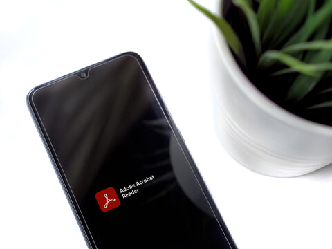 Modern minimalist office workspace with black mobile smartphone with Adobe Acrobat Reader app launch screen with logo on white background