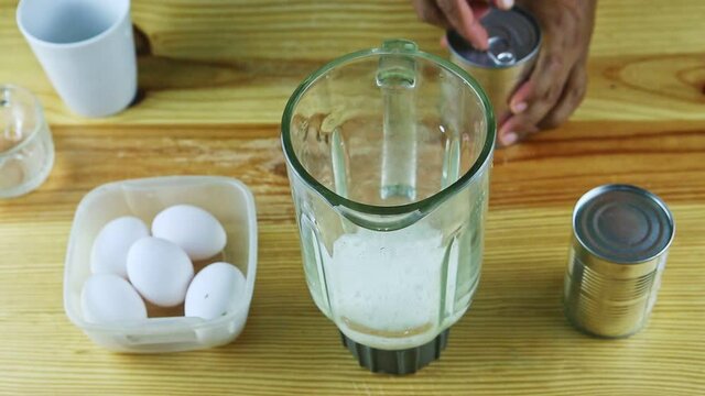top view on man by hands pours canned milk into blender chalice with daily milk