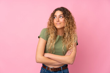 Young blonde woman with curly hair isolated on pink background making doubts gesture while lifting the shoulders
