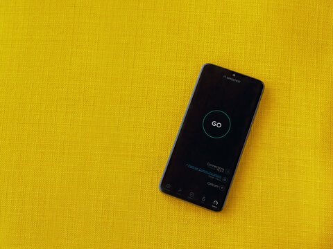 Lod, Israel - July 8, 2020: Speedtest app launch screen with logo on the display of a black mobile smartphone on a yellow fabric background. Top view flat lay with copy space.