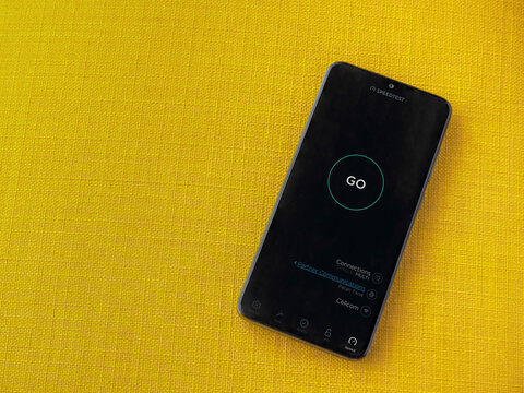 Lod, Israel - July 8, 2020: Speedtest app launch screen with logo on the display of a black mobile smartphone on a yellow fabric background. Top view flat lay with copy space.