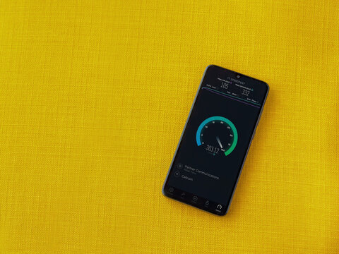 Lod, Israel - July 8, 2020: Speedtest app launch screen with logo on the display of a black mobile smartphone on a yellow fabric background. Top view flat lay with copy space.