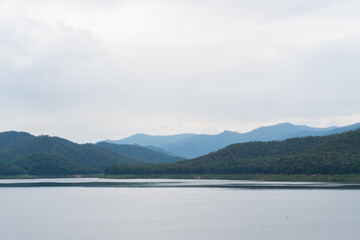 Landscape of the lake dam in the north of Thailand, fertile green forest trees mountain panoramic view with white blue clouds wide winter sky as the abstract background, still and calm water