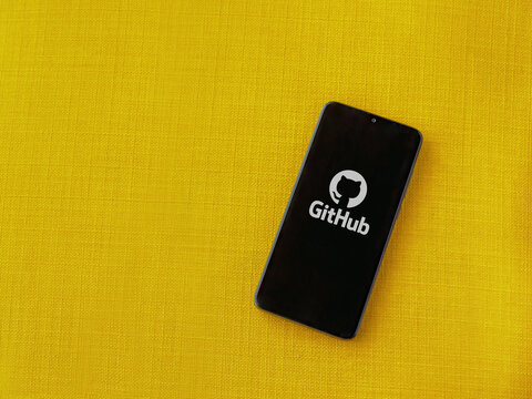 Lod, Israel - July 8, 2020: GitHub app launch screen with logo on the display of a black mobile smartphone on a yellow fabric background. Top view flat lay with copy space.