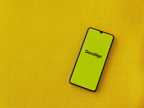 Lod, Israel - July 8, 2020: DocuSign app launch screen with logo on the display of a black mobile smartphone on a yellow fabric background. Top view flat lay with copy space.