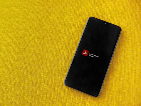Lod, Israel - July 8, 2020: Adobe Acrobat Reader app launch screen with logo on the display of a black mobile smartphone on a yellow fabric background. Top view flat lay with copy space.