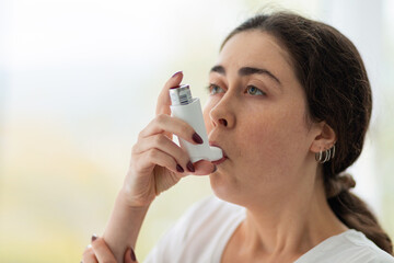 Asthma. Portrait of a young woman inhaling medicine. Blurry background. Copy space