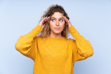 Young blonde woman with curly hair isolated on blue background having doubts and thinking