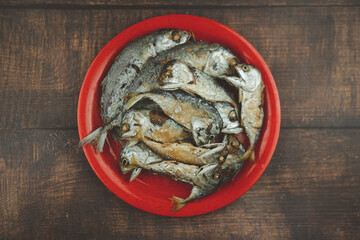 Fried many sizes mackerel fishes on red plate.