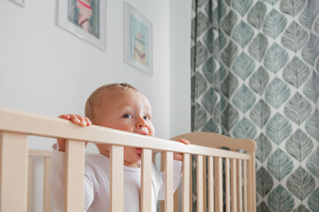 Blond cute little baby biting wooden bed headboard