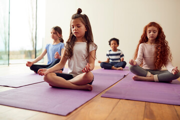 Group Of Children Sitting On Exercise Mats And Meditating In Yoga Studio - Powered by Adobe