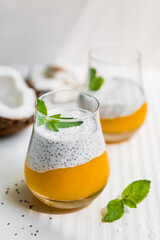 Chia pudding with mango puree in glasses with a sprig of mint and coconut on a white background