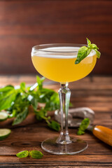 Gin-based citrus cocktail with cucumber and basil in a glass on a wooden background with basil leaves and slices of cucumber