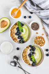 Two banana and avocado smoothie bowls with granola, coconut, honey, chia seeds, blueberries, decorated with a leaf of mint. Top view on a white background.