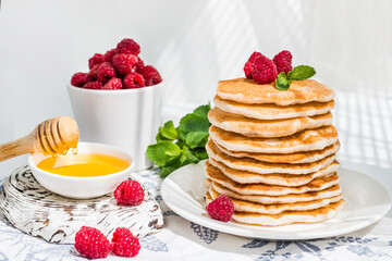Pancakes on a white plate on a white background, decorated with raspberries and a sprig of mint