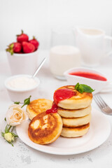 Cottage cheese pancakes with strawberry jam, decorated with a mint leaf on a light background