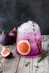 Purple cocktail with figs and thyme sprig on wooden background
