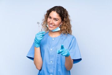 Young blonde woman dentist holding tools isolated on blue background points finger at you