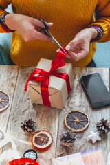 Young woman wrapping christmas present on table with new year deorations