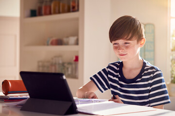 Fototapeta na wymiar Boy Sitting At Kitchen Counter Doing Homework Using Digital Tablet