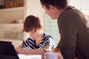 Fototapeta na wymiar Father Helping Son With Homework Sitting At Kitchen Counter Using Digital Tablet Together