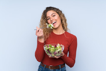 Young blonde woman with curly hair holding a salad over isolated wall