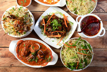 Assorted indian food chicken gravy,chicken biryani, pepper chicken, noodles, fried rice and dal tadka on wooden background. Dishes and appetizers of indian cuisine