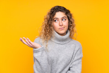 Young blonde woman with curly hair wearing a turtleneck sweater isolated on yellow background unhappy for not understand something