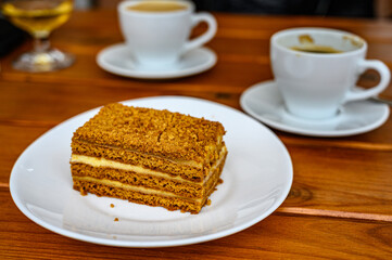 a piece of puff honey cake on a plate and a cup of coffee on a blurred background in a cafe.