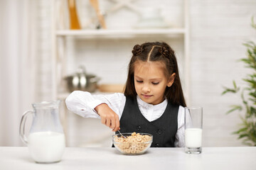 smiling cute little girl in school uniform having breakfast: cereal with the milk in the kitchen. healthy breakfast