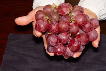 Mano de mujer mostrando un racimo de uva roja.