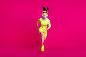Full length body size photo of female runner jumping high running forward wearing face mask isolated on bright fuchsia color background