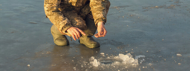 Naklejka premium The guy on the winter fishing at the hole catches a small fishing pole. Closeup of a hand with a winter fishing rod.