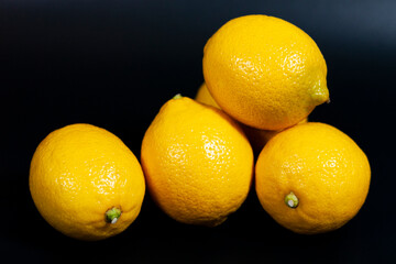 A pile of yellow lemons stacked on a dark background.