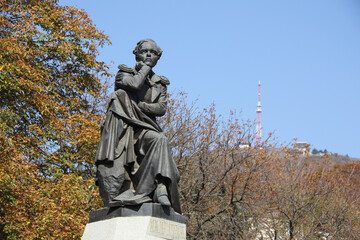 Bronze sculpture to famous Russian poet Mikhail Yuryevich Lermontov against the background of autumn Pyatigorsk and mount Mashuk.