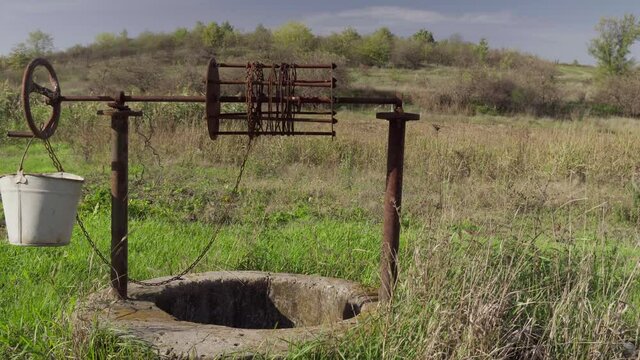 An old water well on rural homestead. An abandoned well in the middle of green grass and trees.