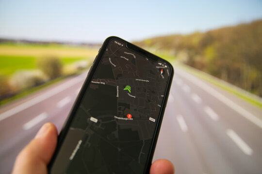 Viersen, Germany - July 9. 2020: Closeup of hand holding mobile phone in car with radar warning speed check app. Blurred highway background.