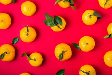 Fresh clementines with leaves patterned on a red background, top view