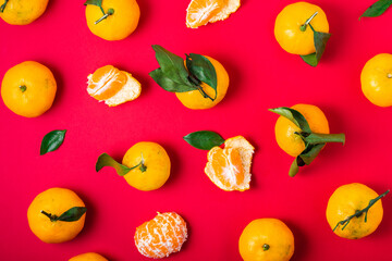Fresh clementine slices and whole fruits with leaves patterned on a red background, top view