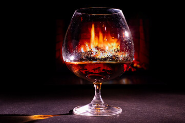 Close-up on a glass of brandy in the dark on the background of the fireplace