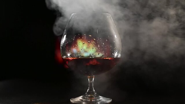 A glass of brandy and cigar smoke in the dark on the background of the fireplace. Gentlemen's club concept