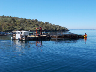 man working on fish farm with ponds nets boats at sea with mountain background