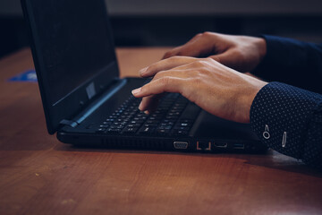Man does homework in the evening, uses a laptop while sitting at a table in a dark room at home. Distance learning at home during quarantine